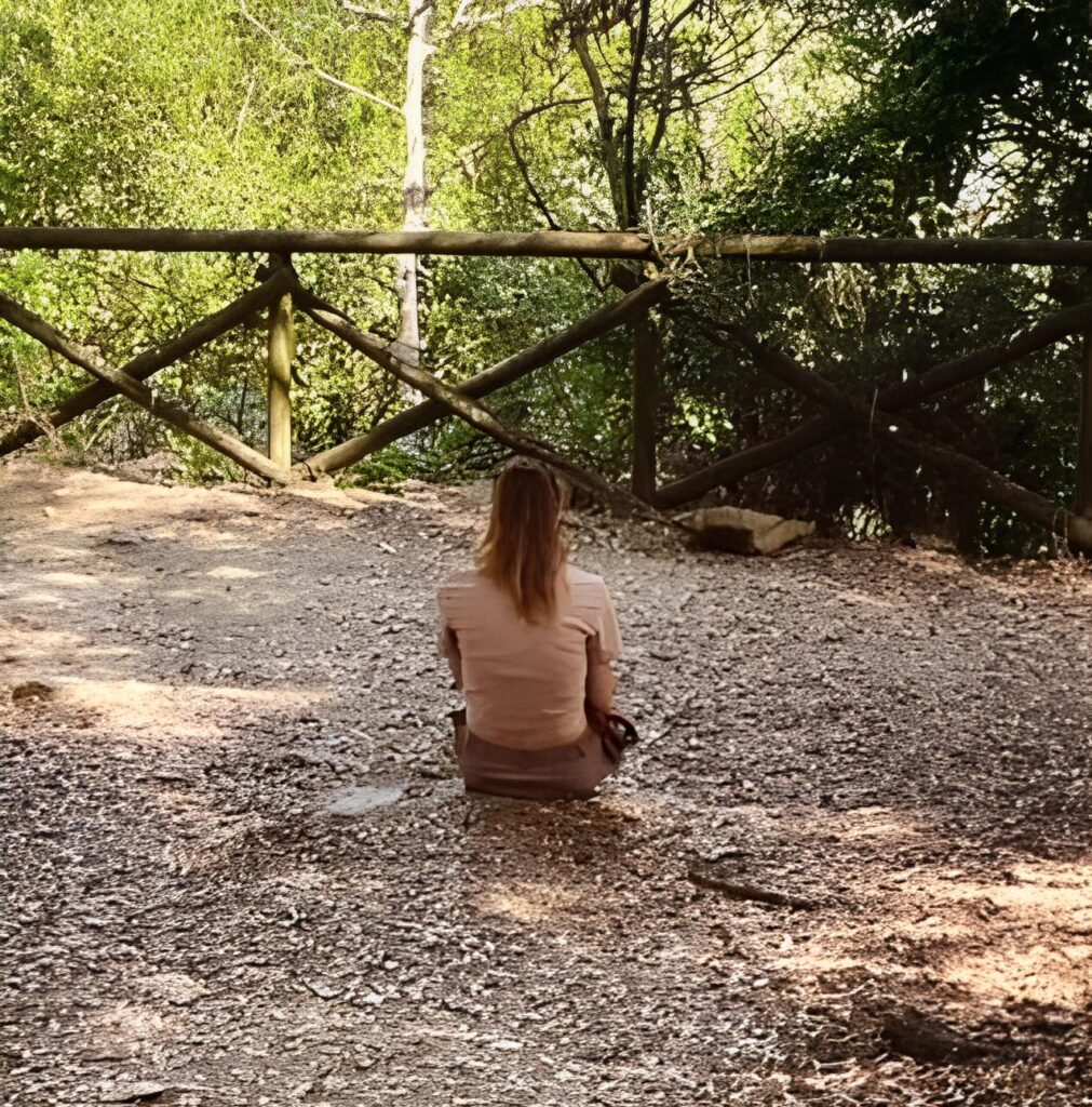 Una donna seduta di spalle in contemplazione della natura intorno a lei.